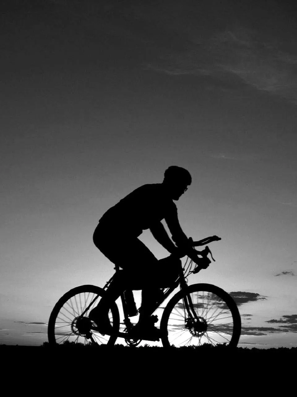 Silhouette of a cyclist riding along a ridge at dusk.