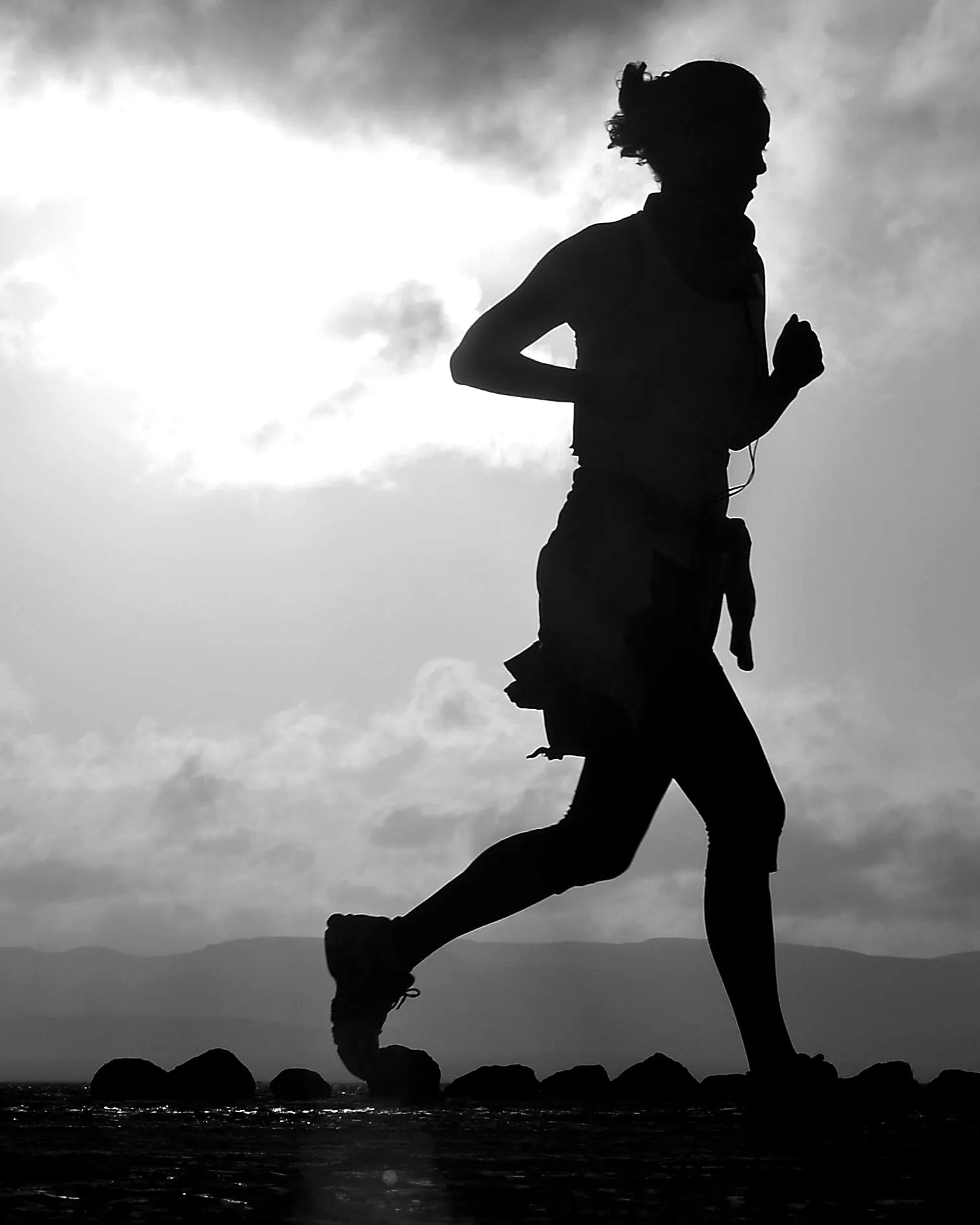 Silhouette of a runner against a bright, cloudy sky, with two cyclists far in the distance.