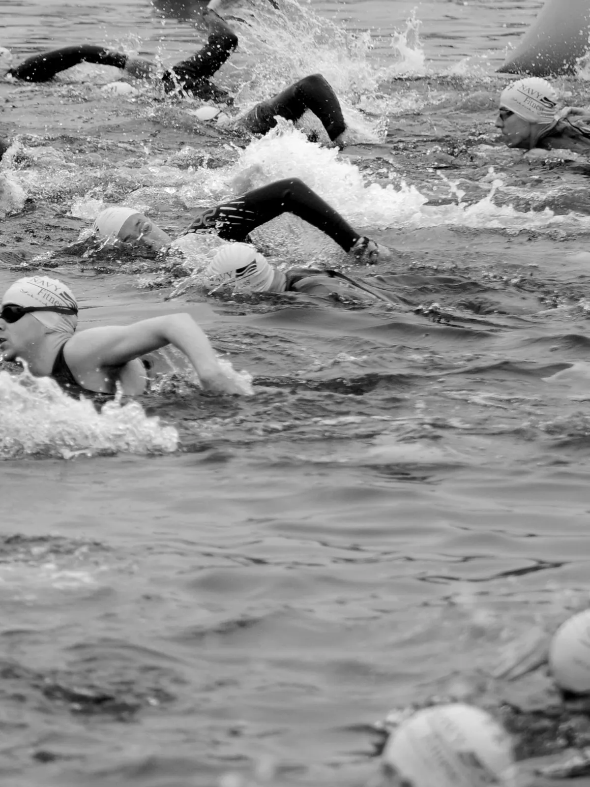 Triathletes in swim caps churning through open water at the start of a race.